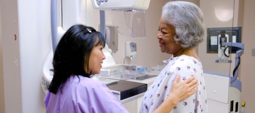 nurse prepares a woman in hospital gown for her mammogram