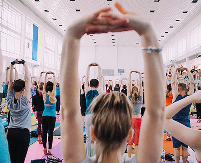 large room full of people stretching above their head in a yoga class