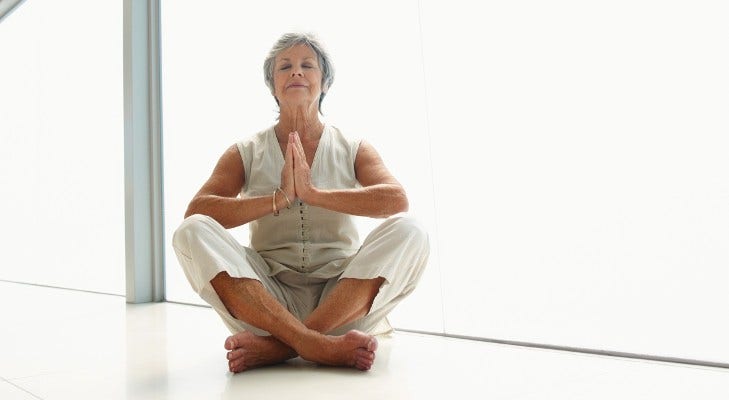 senior woman does yoga in white room