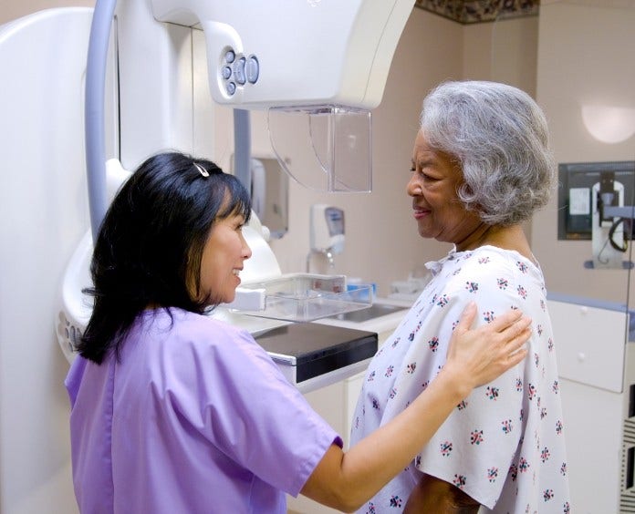 nurse preparing woman in hospital gown for mammogram