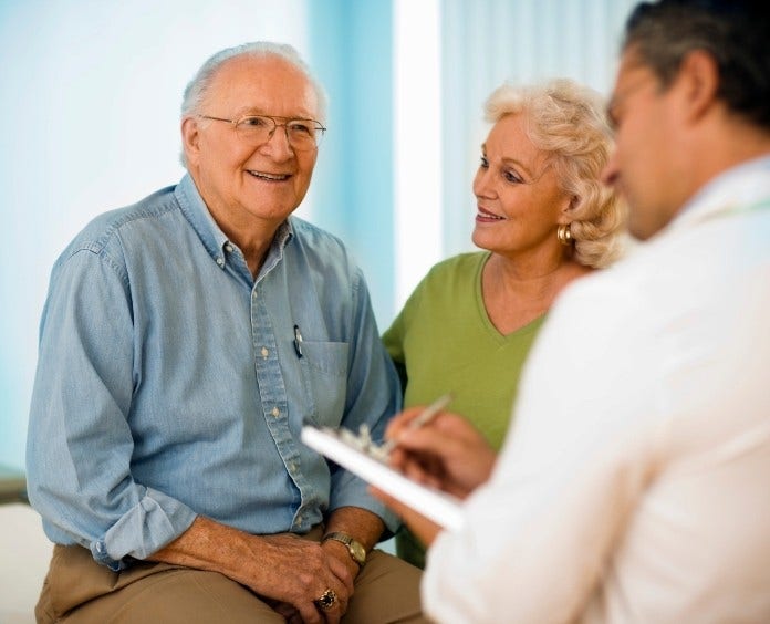 smiling senior couple talk with their doctor 