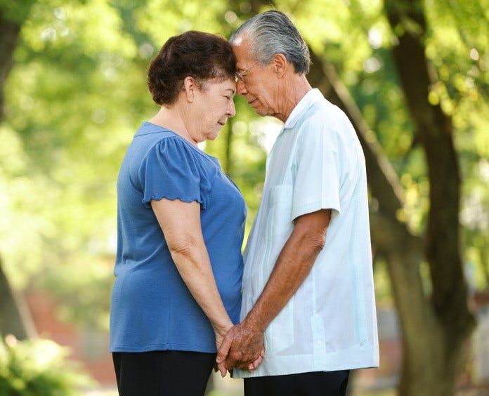 senior asian couple clasping hands and touching foreheads outside
