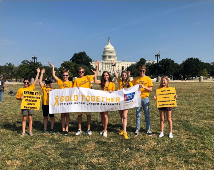 group of people all wearing gold shirts standing in front of capital