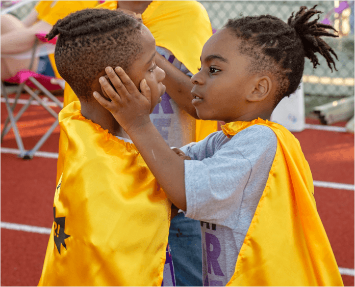 two black male children hugging wearing gold capes