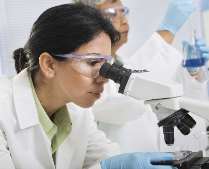female researcher in goggles looking into a microscope in lab