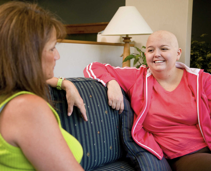 bald female cancer patient talking with woman on couch
