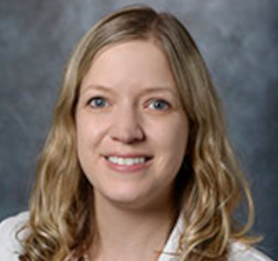 White woman with wavy blonde hair, longer than shoulders, wearing white lab coat